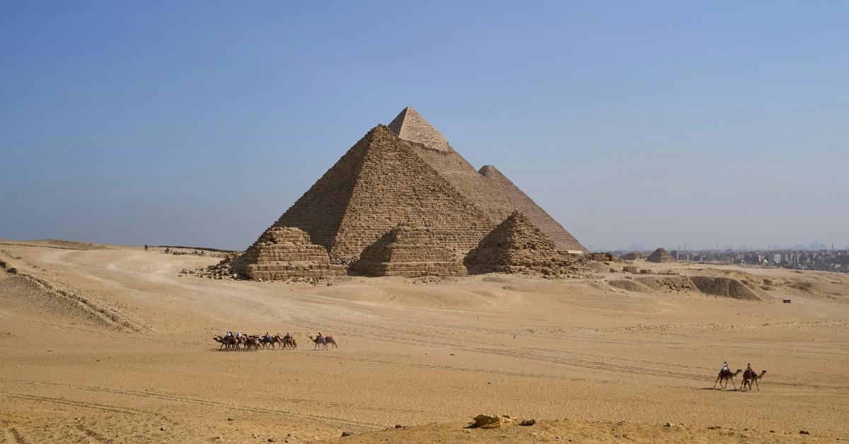 The Giza pyramid complex stands in the background as tourist ride around it on camels